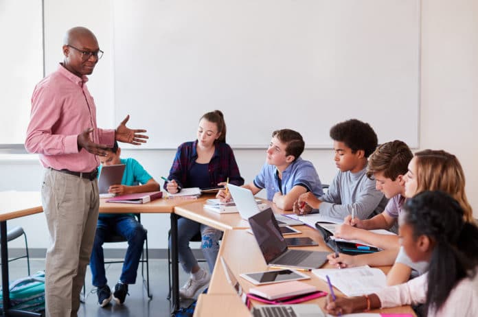 High School Teacher Talking To Pupils Using Digital Devices In Technology Class